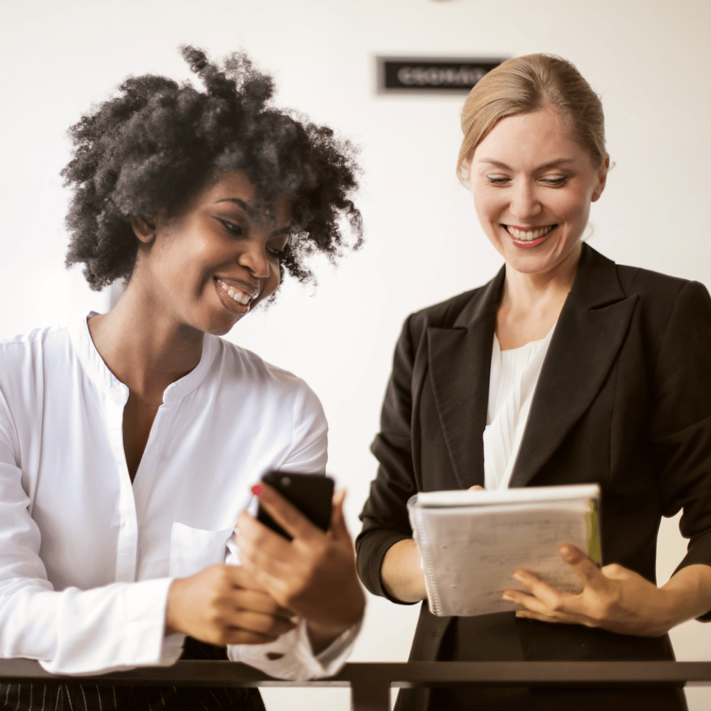 two women looking at phone and paper